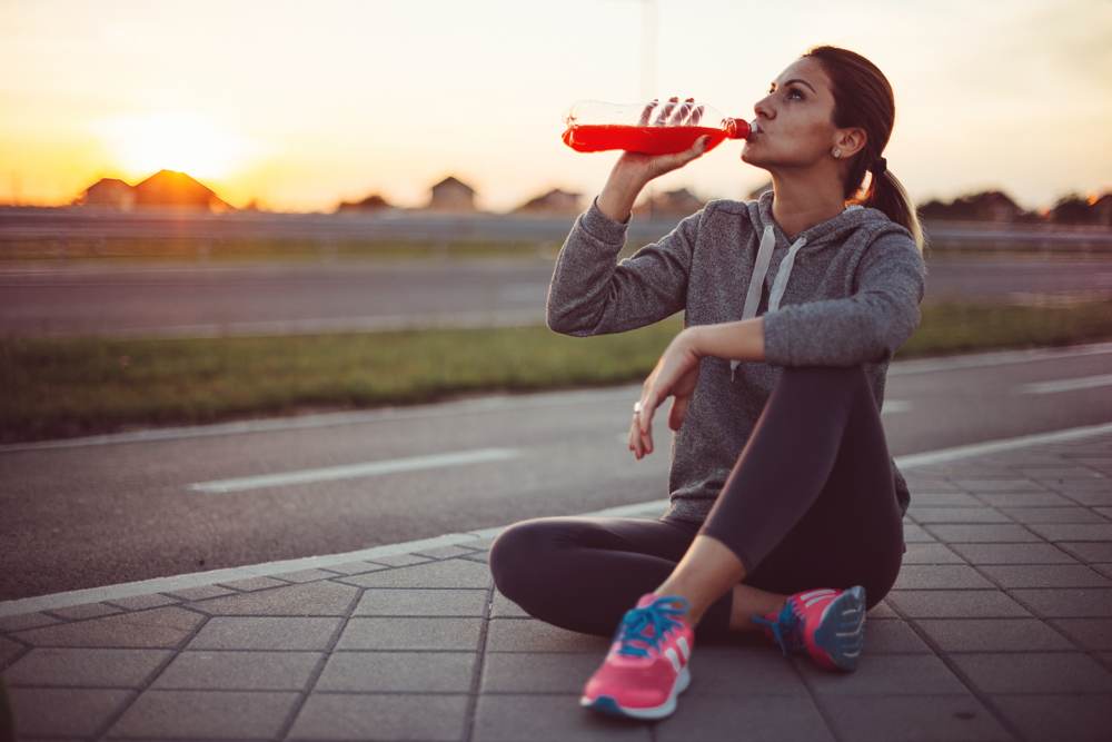 person-sitting-on-sidewalk-drinking-from-water-bottle